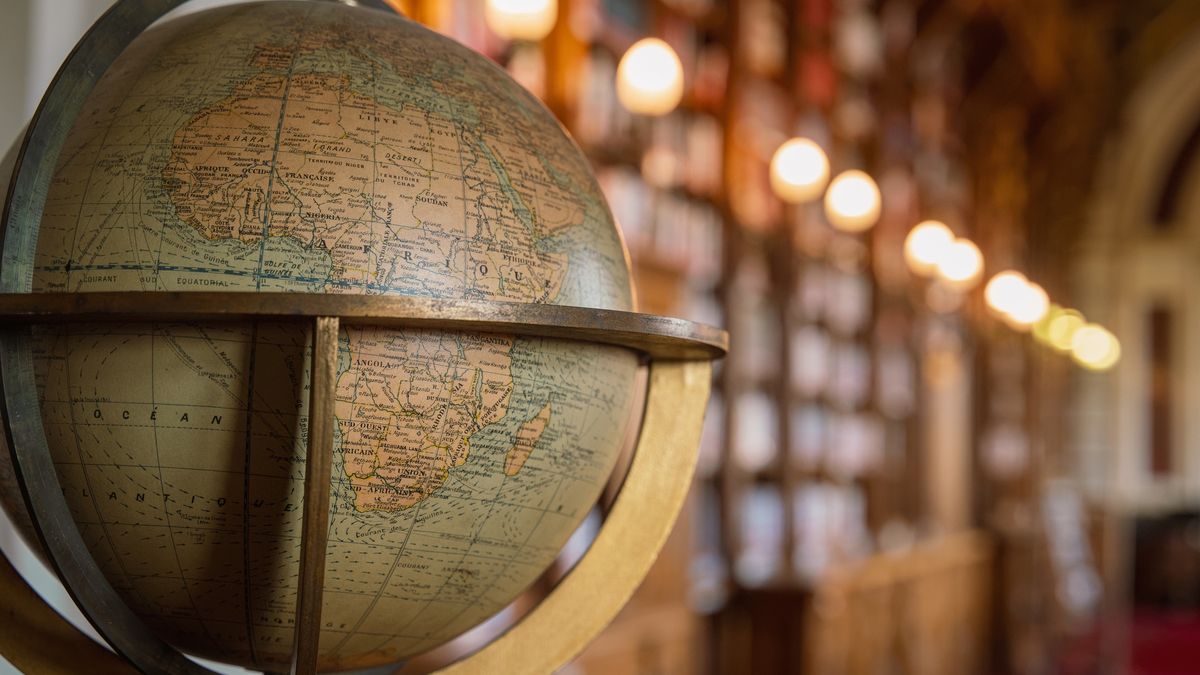 Antique Globe in Historic Library
Vintage terrestrial globe mounted in a brass stand sits prominently in the foreground of an elegant historic library, with rows of warm Edison bulb lighting illuminating towering wooden bookshelves in the background.
Jacques Julien