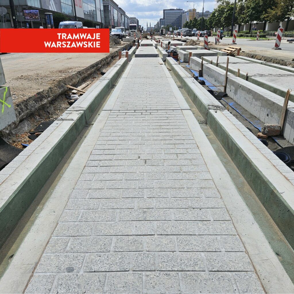 Nowa nawierzchnia tramwajowa z kostki brukowej w trakcie budowy, otoczona wykopami i betonowymi elementami.