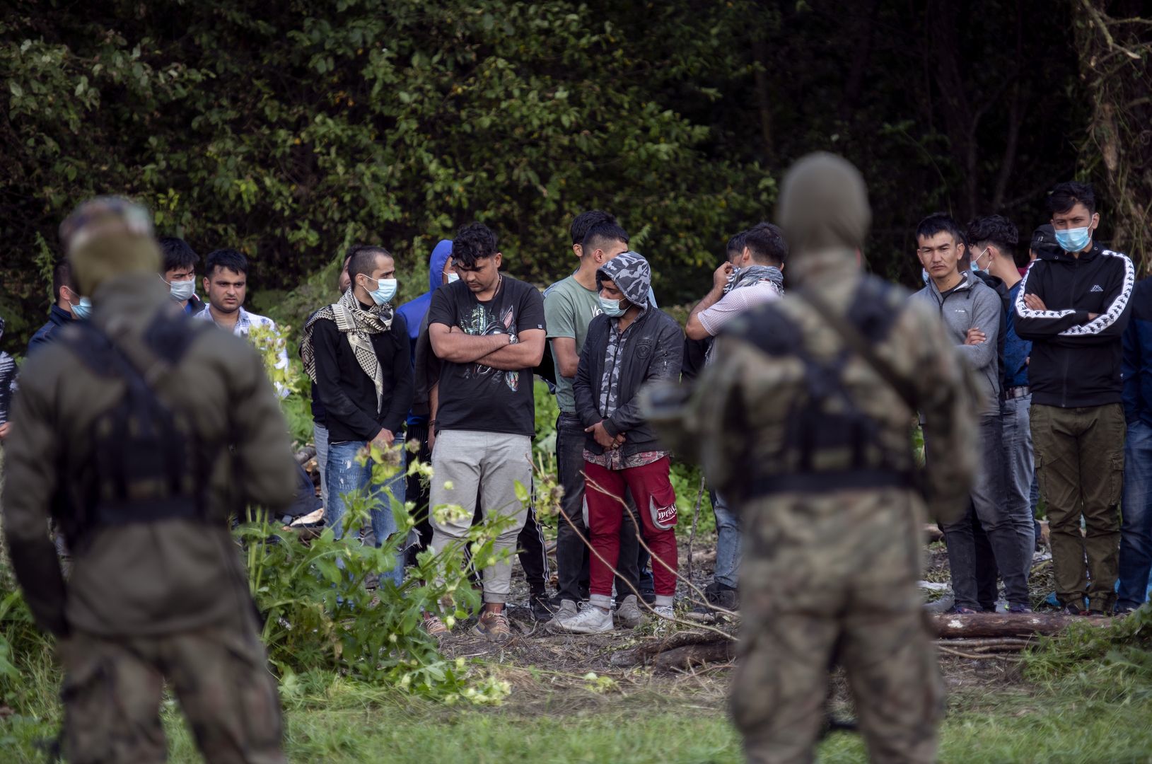 Usnarz Gorny, woj. podlaskie, 12.08.2021. W zwiazku z rosnaca z dnia na dzien iloscia nielegalnych imigrantow przekraczajacych bialorusko-polska granice, Straz Granicza wzmocnila swoje dzialania na granicy z Republika Bialorus na terenie wojewodztwa podlaskiego. Tylko w  ciagu ostatniego weekendu (6-8.08.2021) zatrzymano 349 osob - glownie Irakijczykow i Afganczykow - usilujacych nielegalnie dostac sie do Polski z Bialorusi. Wg. roznych zrodel, imigranci samolotami dostaja sie do Minska, a stamtad sa przewozeni przez bialoruskie sluzby nad granice z Litwa i Polska. Jest to elementem tzw. wojny hybrydowej. N/z wojsko pilnuje zatrzymanych przy granicy z Bialorusia nielegalnych imigrantow, w tym kobiet i dzieci