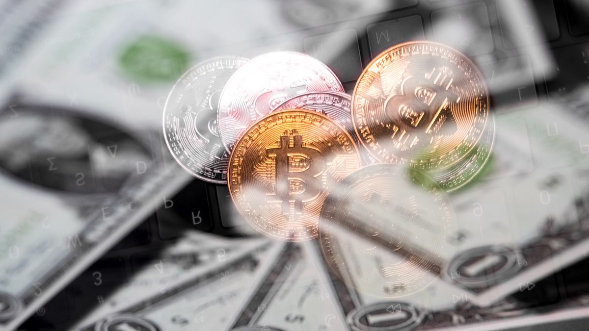 Physical representations of Bitcoin and dollar bills appear as the background on a laptop computer screen in this photo illustration in Athens, Greece, on February 6, 2026. (Photo by Nikolas Kokovlis/NurPhoto via Getty Images)