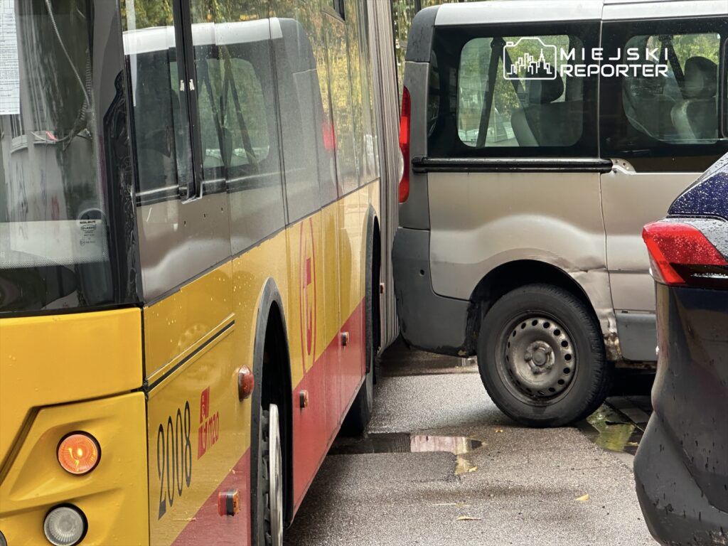 Żółty autobus komunikacji miejskiej zbliża się do szarego dostawczego samochodu zaparkowanego na wąskiej ulicy.