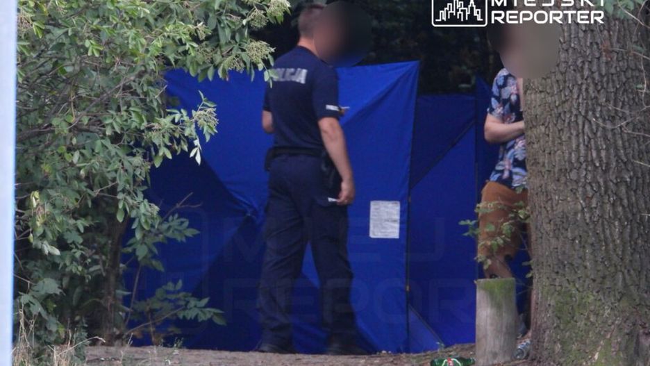 Policjant rozmawia z mężczyzną przy niebieskim namiocie w leśnej okolicy. W tle widoczne śmieci.
