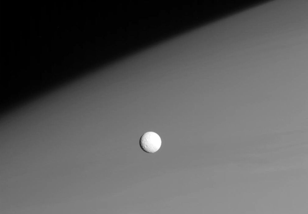 Niewielki lodowo-skalisty księżyc Mimas (średnica: 396 km) na tle