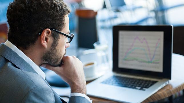 Na zdjeciu mężczyzna wpatrujący się w ekran laptopa, na którym widać wykres