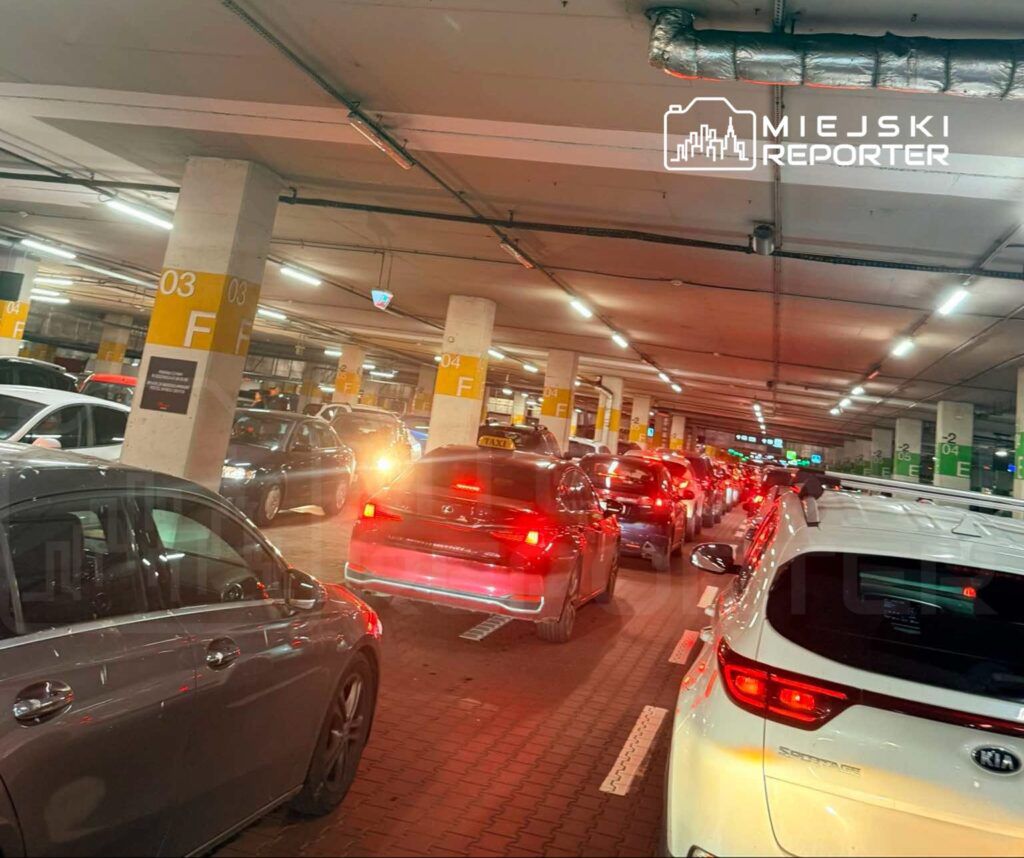 Ruch samochodów w zatłoczonym parkingu podziemnym, z widocznymi światłami hamowania i oznaczeniami miejsc.