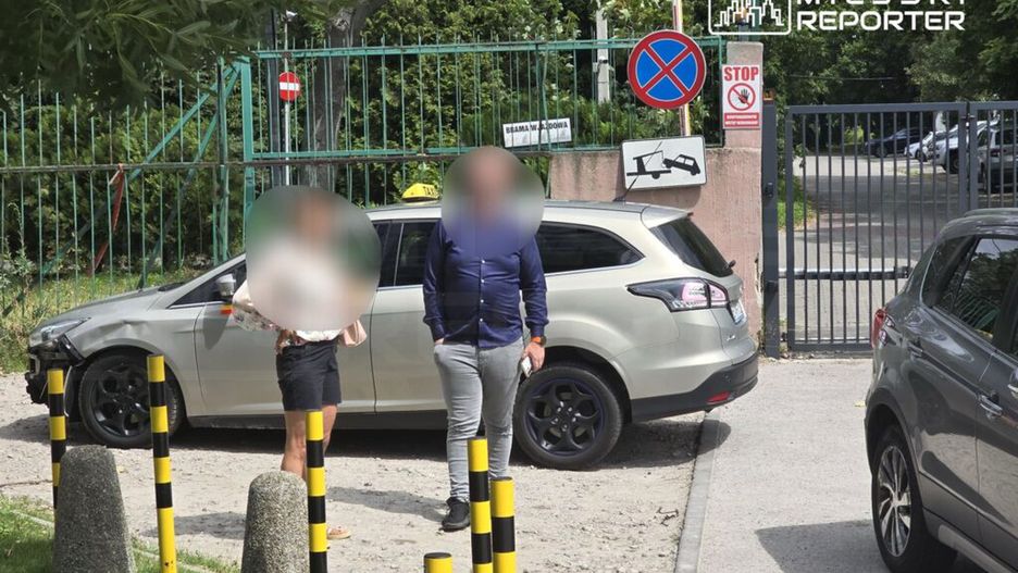 Na zdjęciu widoczni są dwaj ludzie stojący obok samochodu zaparkowanego przy bramie. W tle znajdują się znaki drogowe, w tym zakaz zatrzymywania się oraz oznaczenie strefy, gdzie pojazdy mogą być odholowane. Obraz ilustruje sytuację związaną z parkowaniem w miejscu niedozwolonym.
