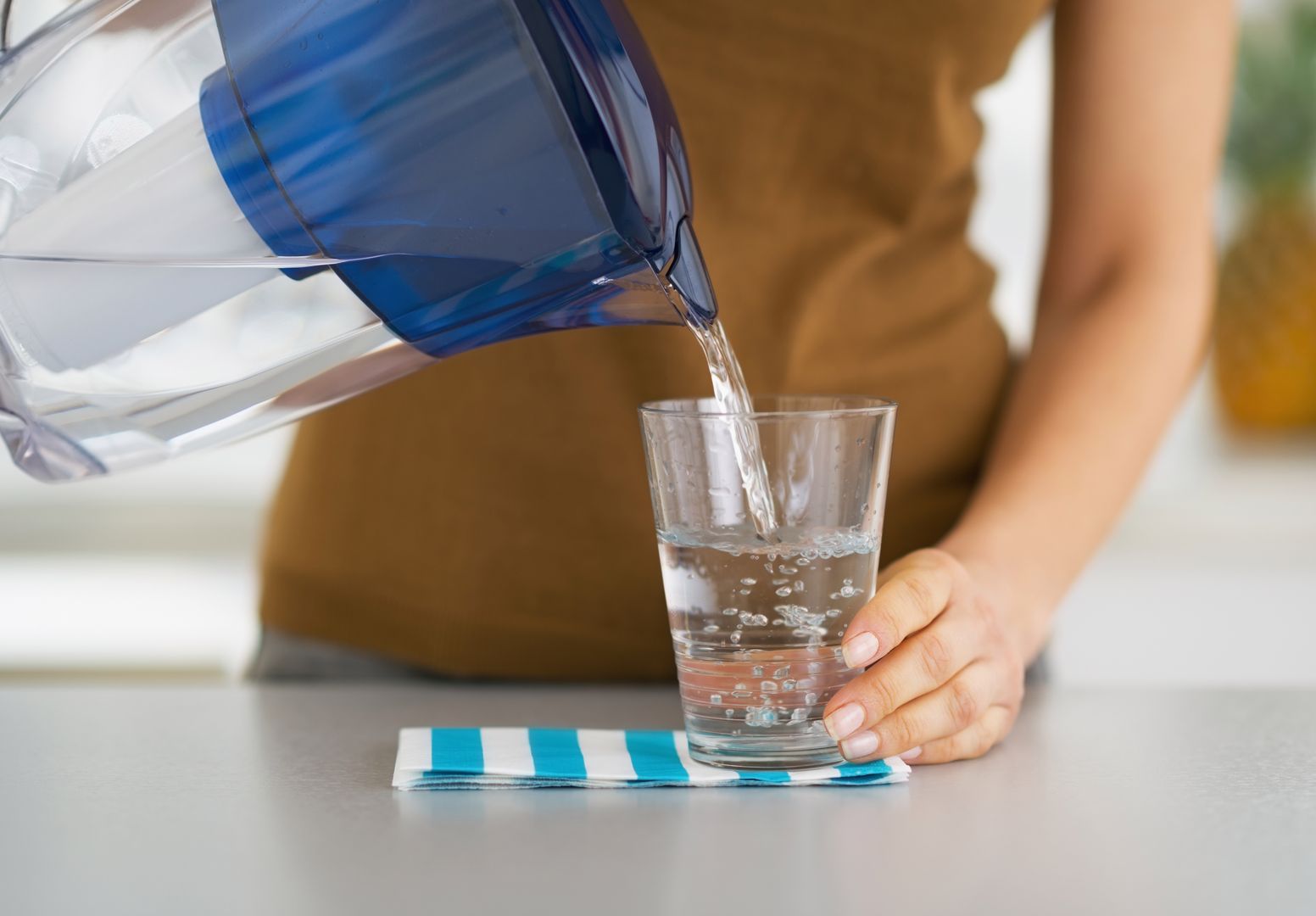 Closeup on housewife pouring water into glass from water filter pitcher 