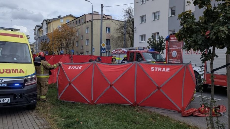 Ratownicy w mundurach ustawiają czerwone namioty wzdłuż ulicy, obok ambulansu i wozu strażackiego.