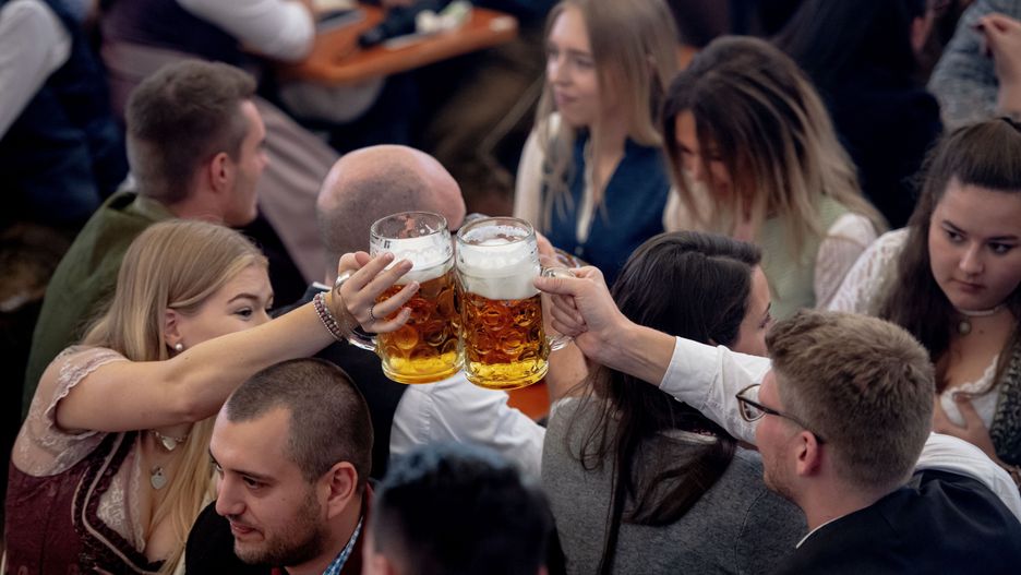 Na zdjęciu uczestnicy Oktoberfestu. Kobieta i mężczyzna zbijają się kuflami nad głowami festiwalowiczów