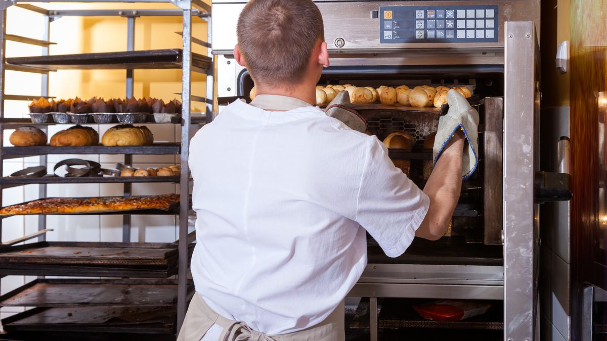 Na zdjęciu piekarz wkładający bułki do pieca
