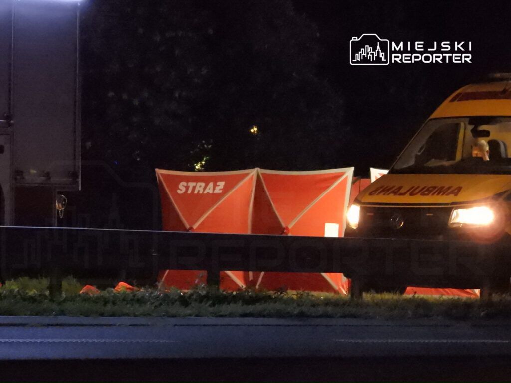 Czerwony namiot z napisem "STRAŻ" ustawiony obok karetki na drodze w nocy.