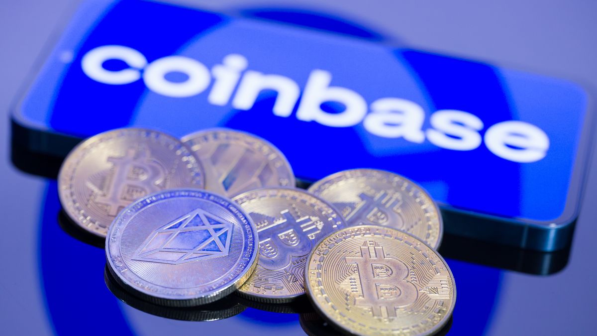 The Coinbase logo is displayed on a mobile phone with crypto coins in this photo illustration in Brussels, Belgium, on February 11, 2026. (Photo by Jonathan Raa/NurPhoto via Getty Images)