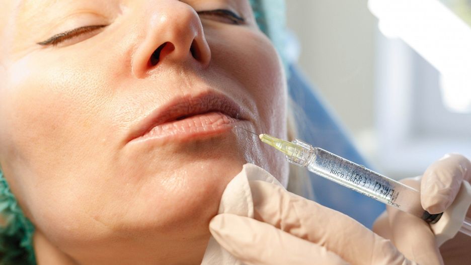 Doctor beautician makes injections in the forehead for patient.