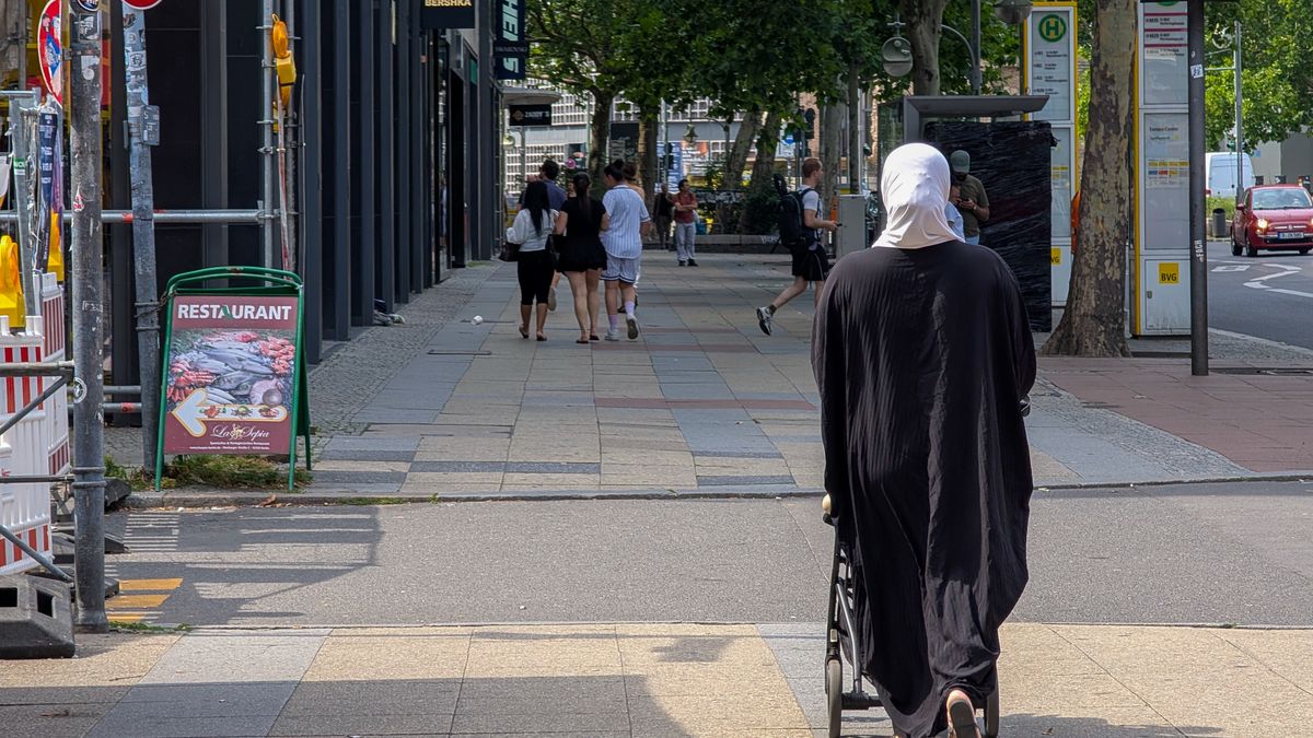 A woman wearing a hijab and black robe walks with a personal shopping trolley along the sidewalk near Marburger Strasse in Berlin, Germany, on July 20, 2025. (Photo by Michael Nguyen/NurPhoto via Getty Images)