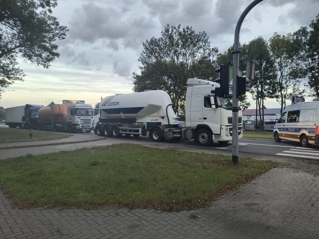 Kierowcy ciężarówek czekają na sygnalizację świetlną przy skrzyżowaniu, obok stoi radiowóz policyjny.