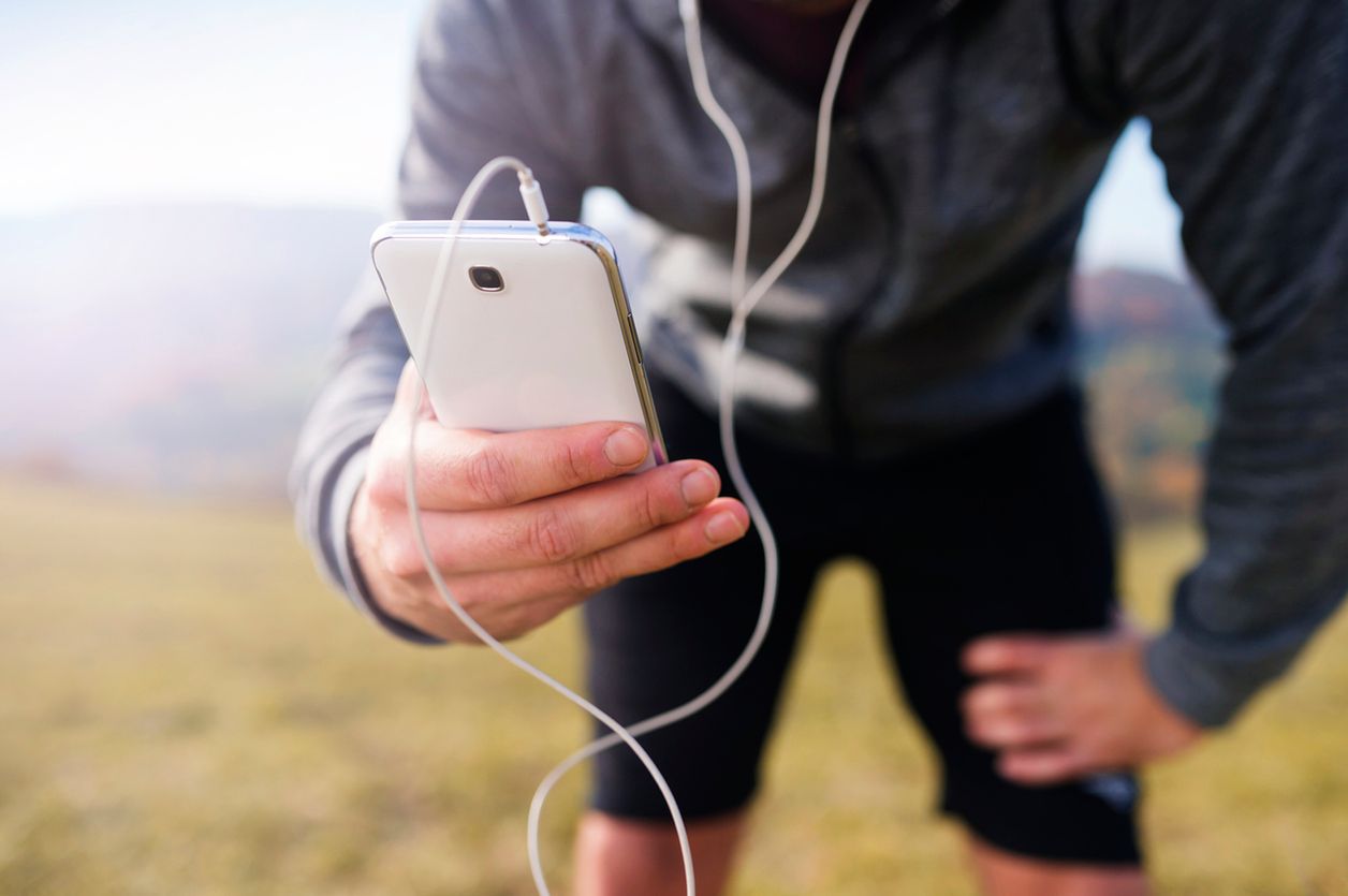 Young handsome runner with smart phone outside in sunny autumn nature 