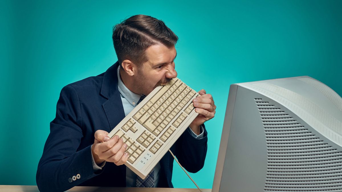 Angry fury businessman breaking keyboard against a blue studio background