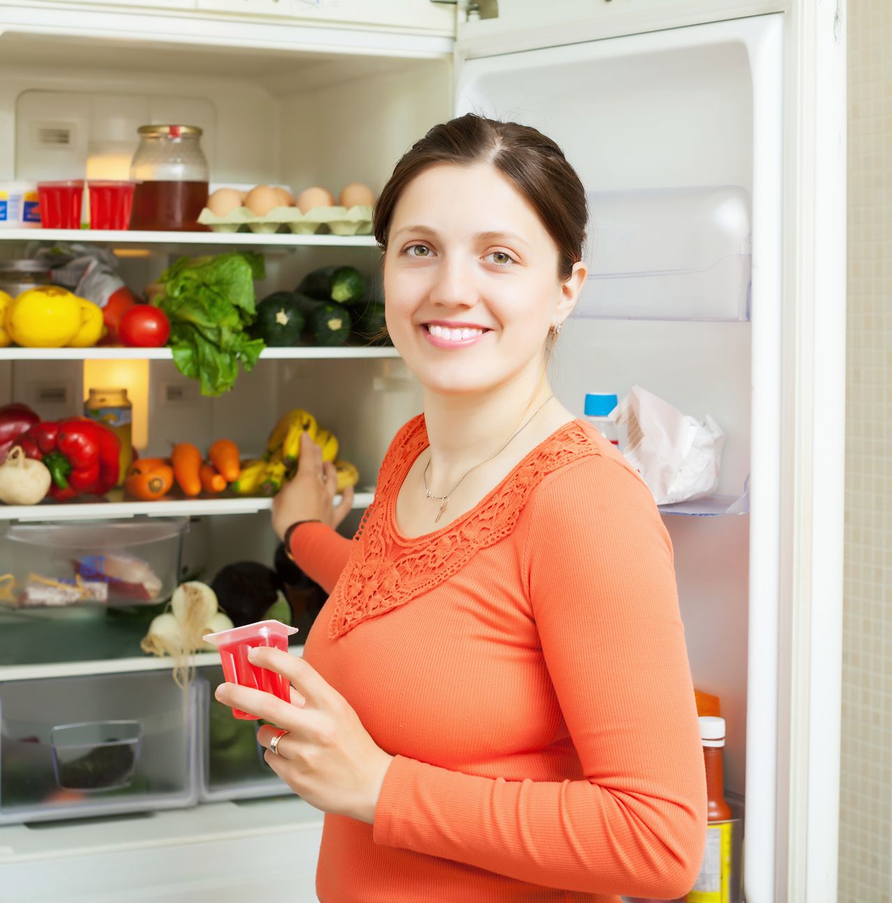 Young woman with fruits jam near fridge at home