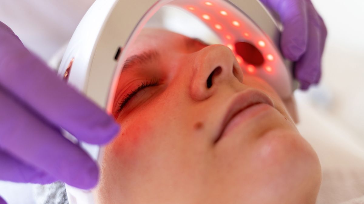 The cosmetologist's hands in medical gloves place a LED lamp with red light over the patient's face.
Tatiana Cheremukhina