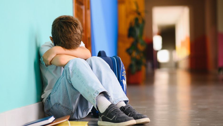 Upset boy sitting at school and crying after bullying by pupils classmates