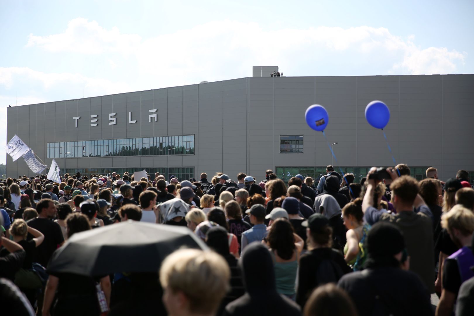 GRUENHEIDE, GERMANY - MAY 11: Environmental activists march in front of the Tesla plant in Gruenheide, southeast of Berlin on May 11, 2024. Activists have come from across Germany to demand a stop to plans by Tesla to expand the factory, which would involve cutting down at least 50 hectares of trees. Some locals also support the protest, citing stress to local groundwater reserves from the factory. (Photo by Maryam Majd/Getty Images)