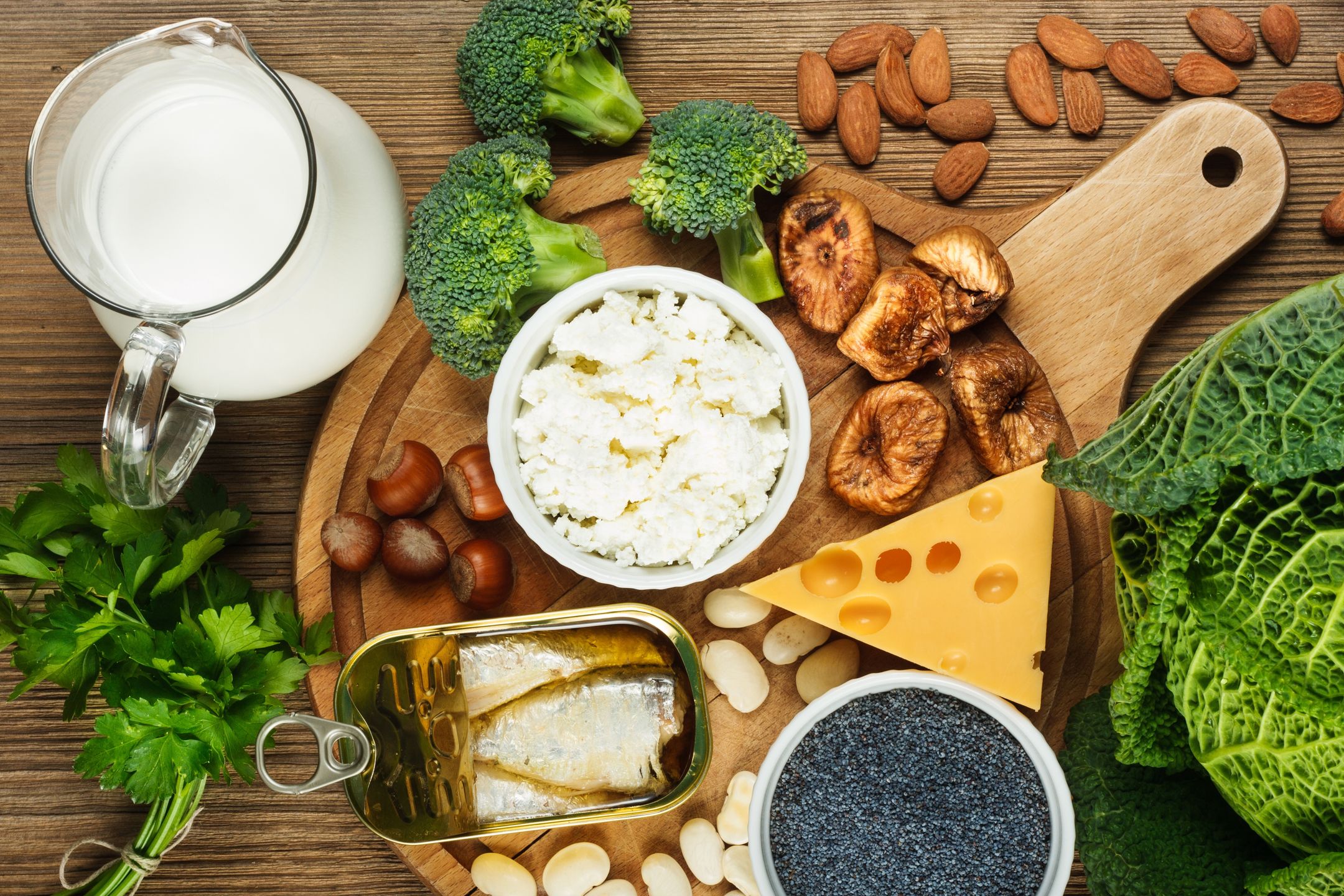Foods rich in calcium such as sardines, bean, dried figs, almonds, cottage cheese, hazelnuts, parsley leaves, blue poppy seed, broccoli, italian cabbage, cheese, milksardines, bean, dried figs, almonds, cottage cheese, hazelnuts, parsley leaves, blue poppy seed, broccoli, italian cabbage, calcium, rich, food, wooden, background, dairy, cheese, yellow, cutting, board, nobody, top, view, vitamin, fish, D, fruit, vegetable, natural, health, healthy, source, collection, milk