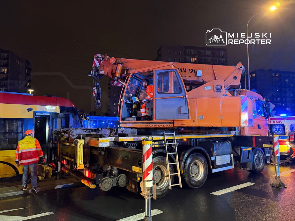 Ekipa ratunkowa pracuje przy wypadku, używając podnośnika hydraulicznego obok tramwaju na oświetlonej ulicy.