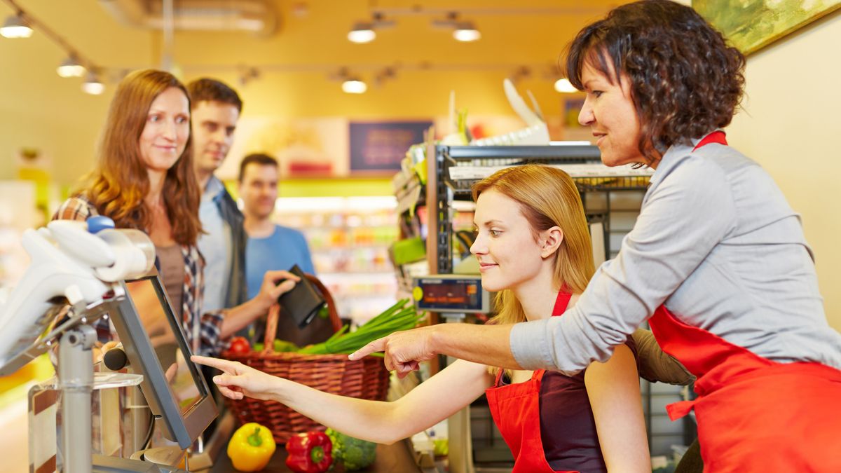 ��ltere Verk��ufer hilft einer neuen Kassiererin an der Kasse im Supermarkt