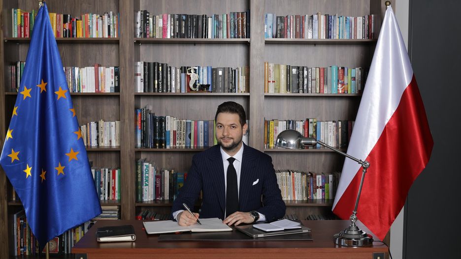 Patryk Jaki na tle książek.