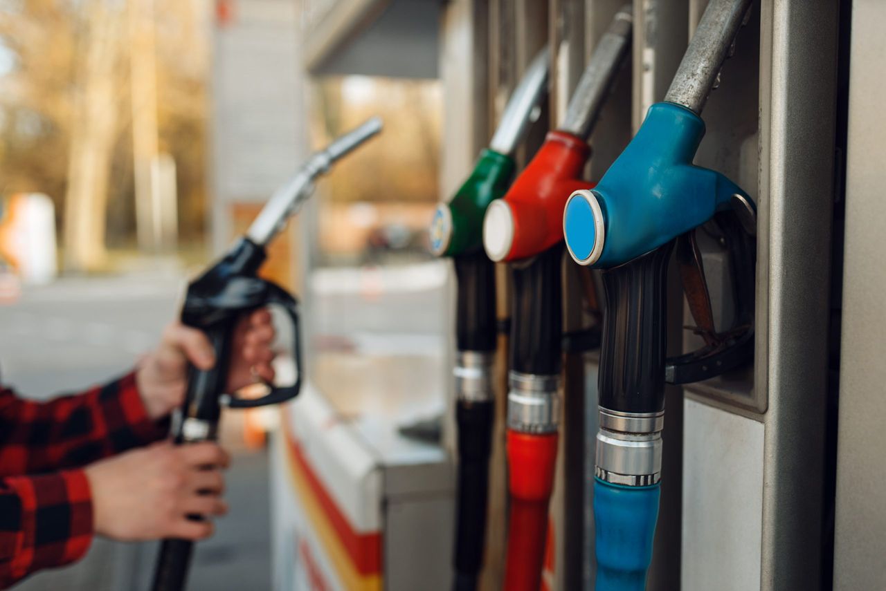 Male worker in uniform takes a gun at a gas station, fuel filling. Petrol fueling, gasoline or diesel refuel service