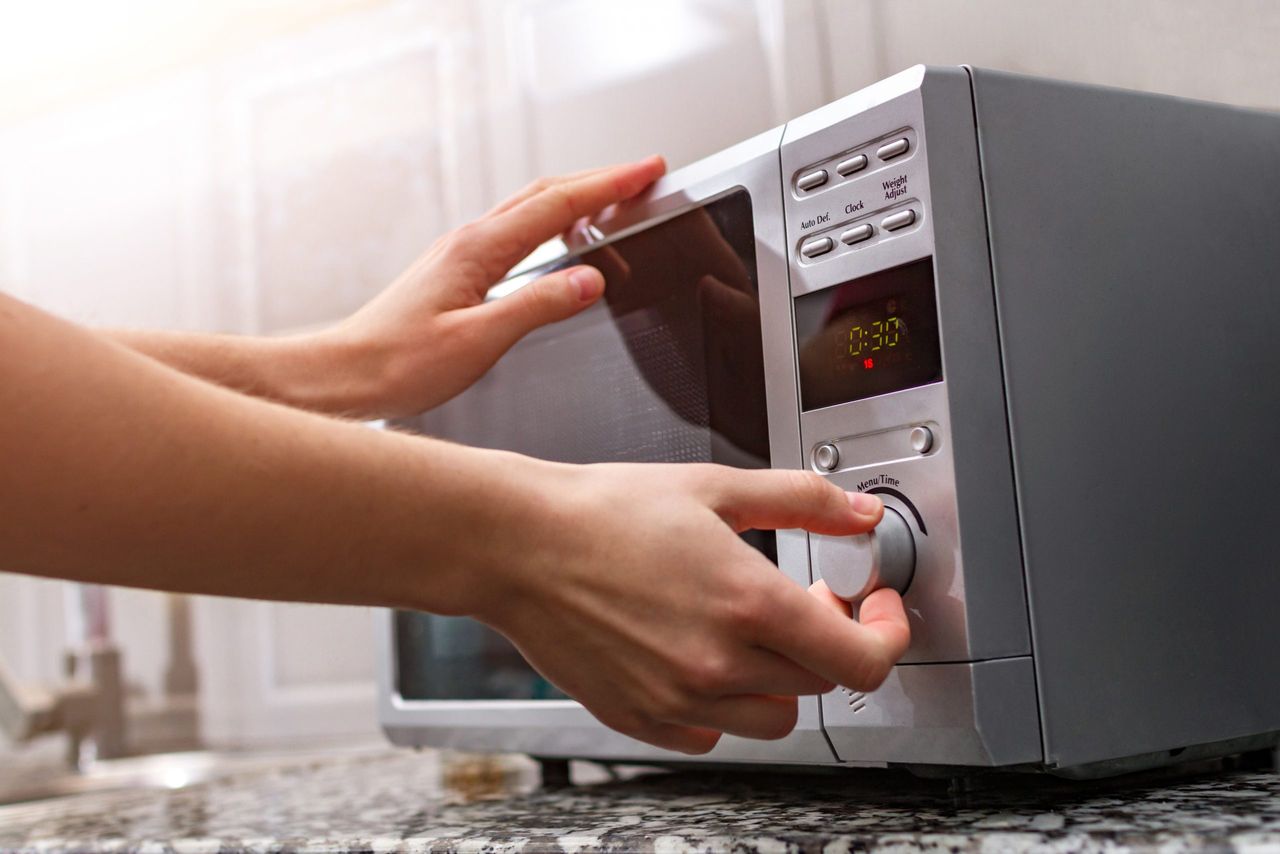 Woman's hand closing the door of the microwave oven and sets the time for heating food