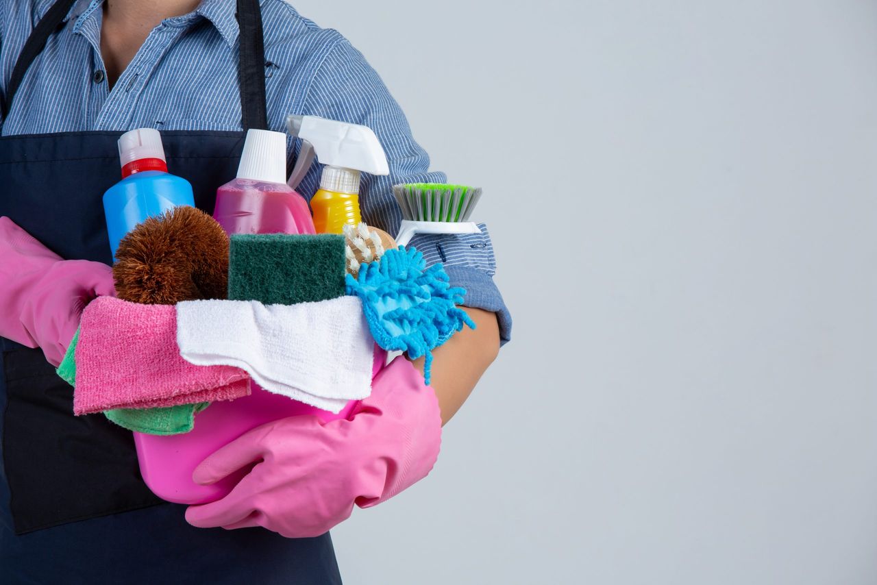 Young girl is holding cleaning product, gloves and rags in the basin on white background