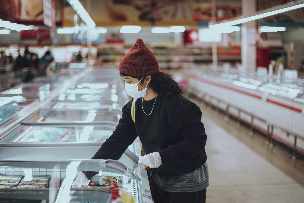 Woman with a medical mask buying frozen food during coronavirus pandemic