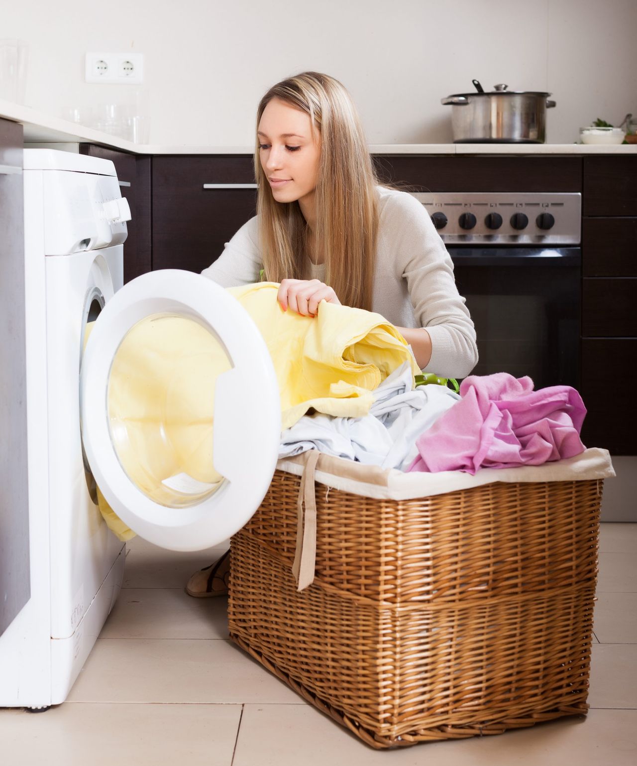 Home laundry. Blonde woman loading clothes into washing machine  in home