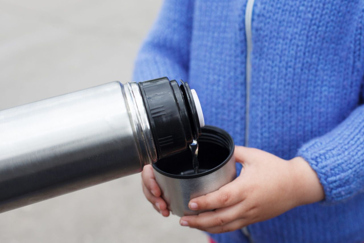 Young girl in a blue knitted sweater drinks tea or coffee from a thermos Cup outdoors