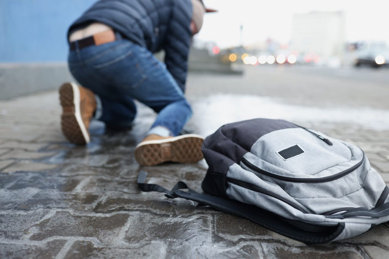 Backpack lying on slippery paving slabs near falling man closeup. Ice injuries concept