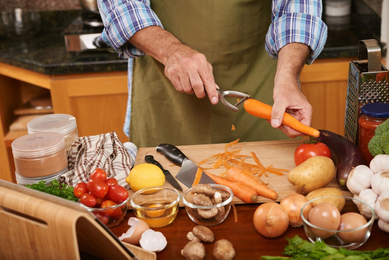 Hands of male cook using peeler when preparing carrot for the dish