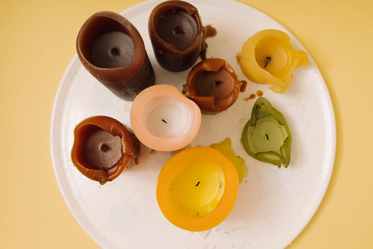 A bunch of burnt wax candles on a white ceramic tray against yellow background. Top view, flat lay.