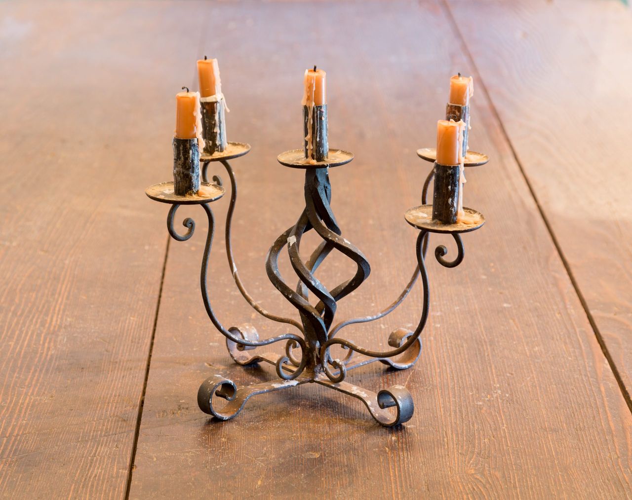 Old iron candlestick holder and candles lit by light from window on old wooden table