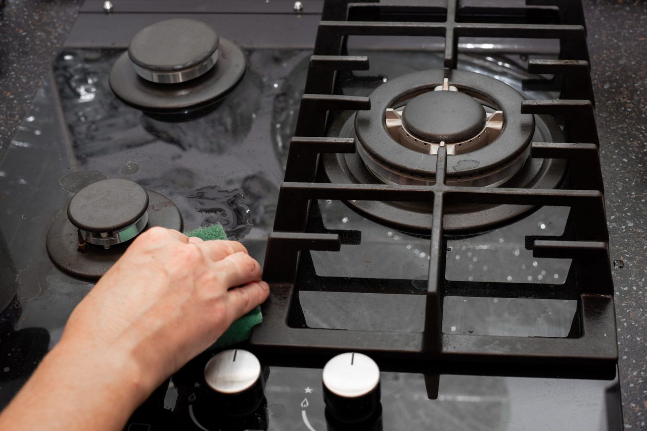 A housewife cleans the kitchen gas glass-ceramic black stove with a sponge. House cleaning.