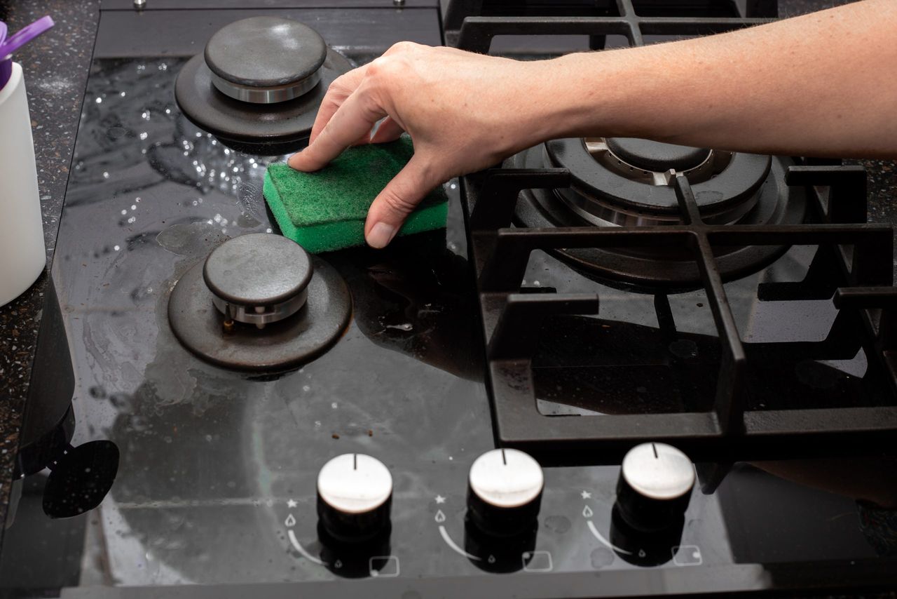 A housewife cleans the kitchen gas glass-ceramic black stove with a sponge. House cleaning.