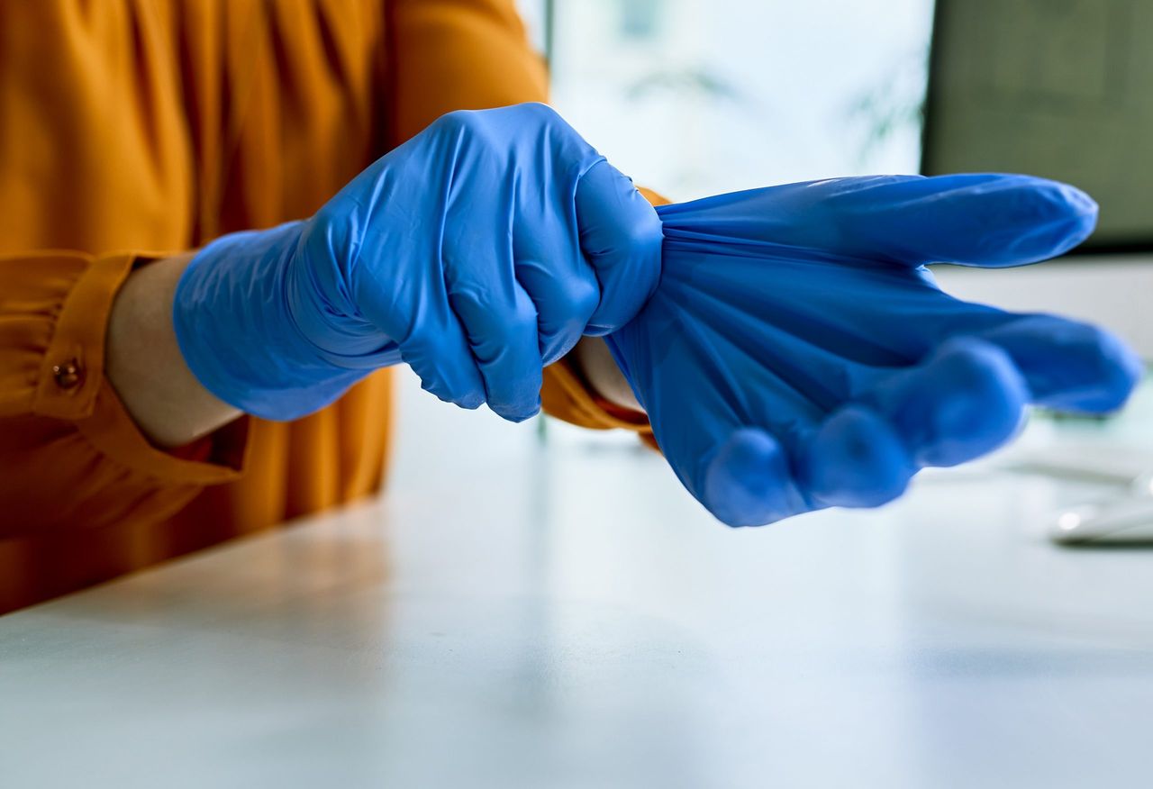 Close-up of businesswoman putting on protective gloves while working in the office.