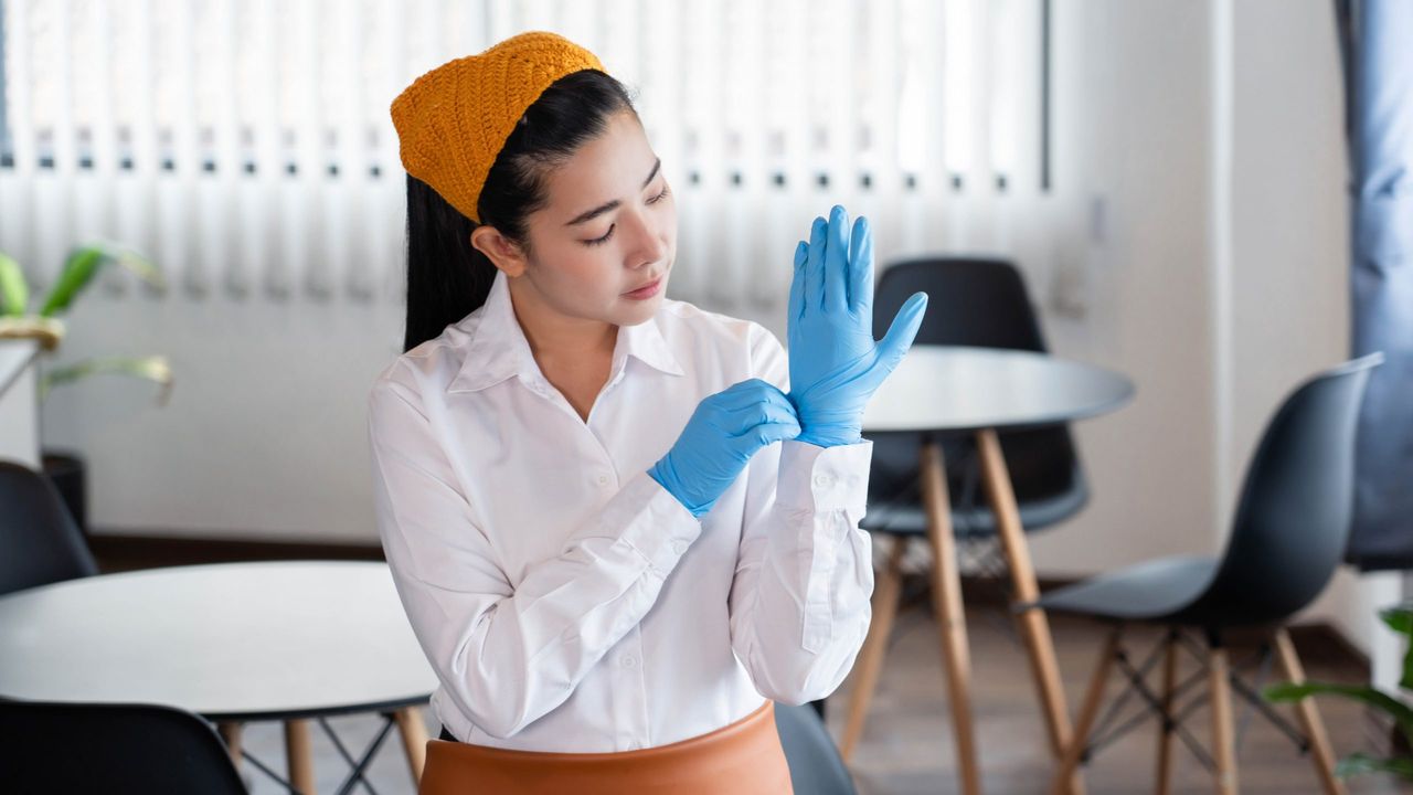 Chore concept a wife house in modest outfit putting on latex gloves to protect herself from the germ before cleaning the office rooms.
