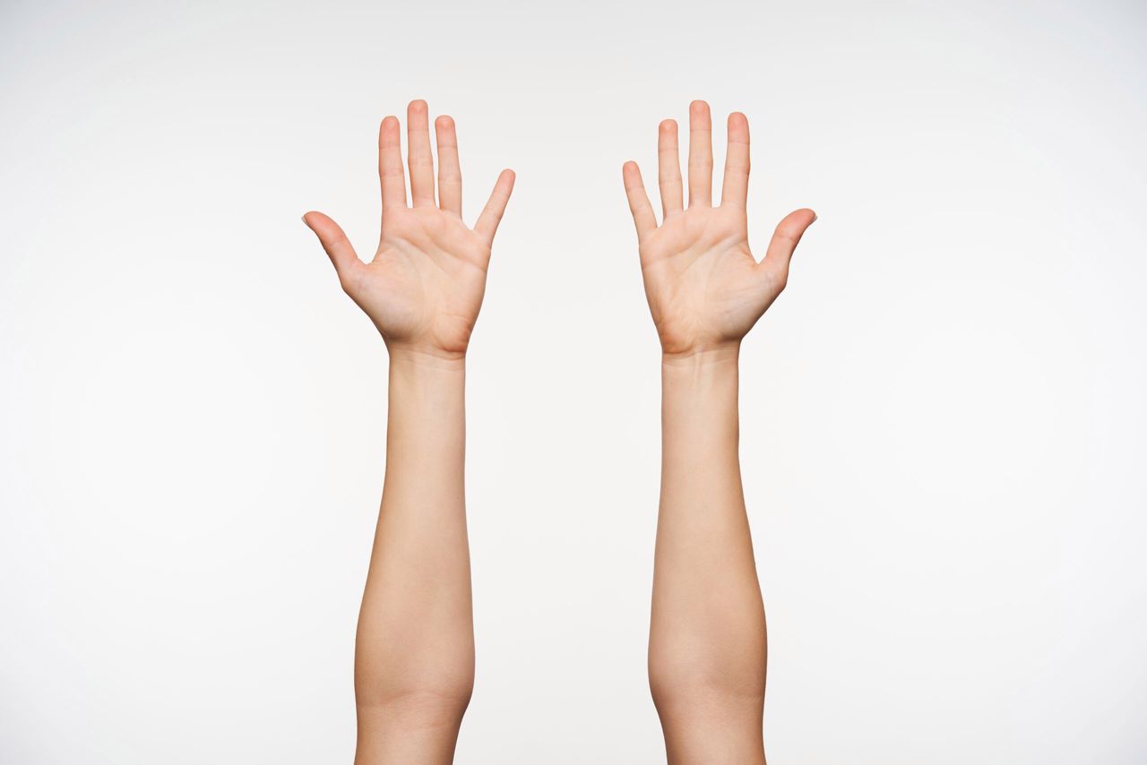 Young pretty fair-skinned female raised hands while isolated over white background, showing her palms to camera and keeping all fingers separetely