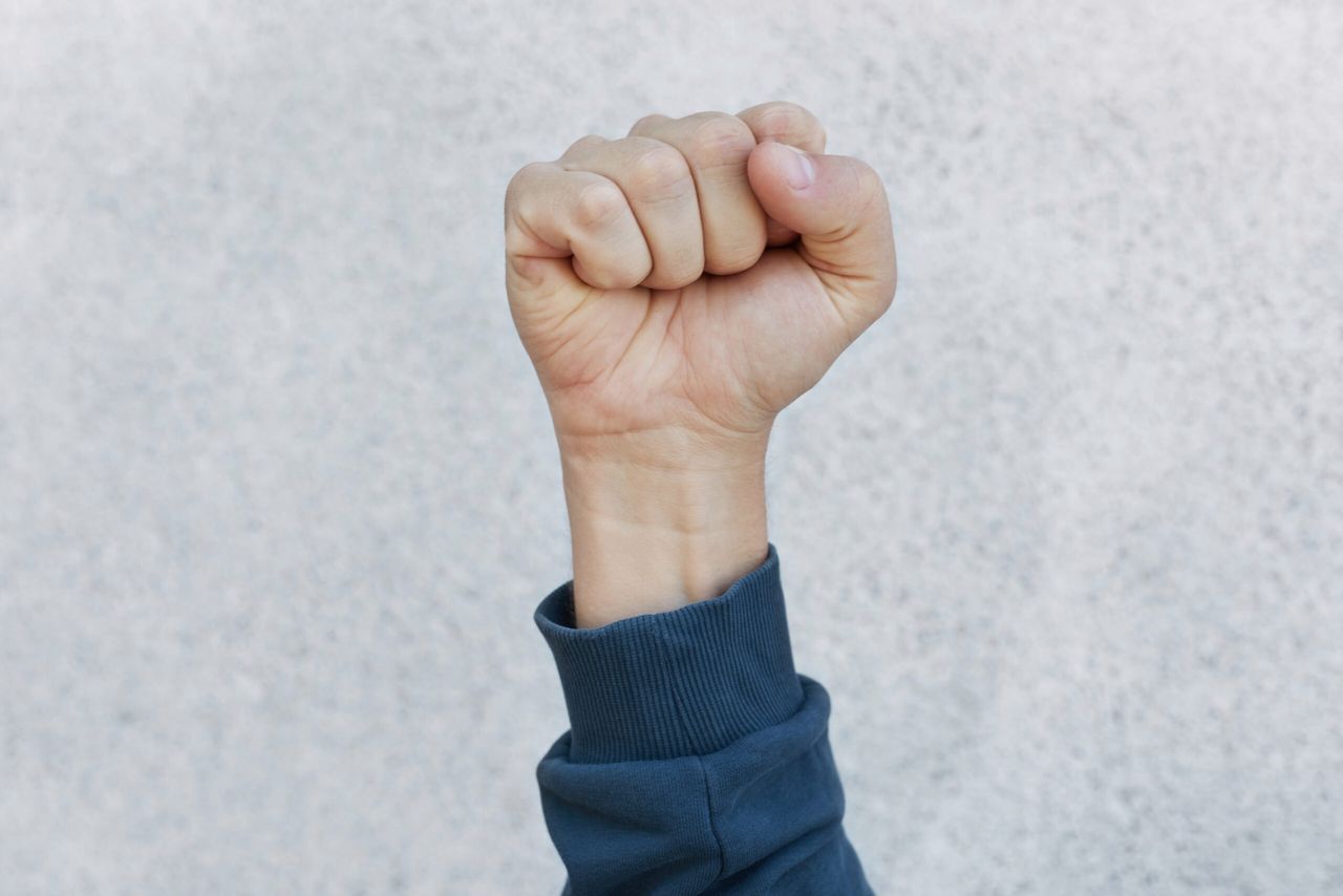 Unknown person protesting, activist fist up during strike. Activism for equal human rights or against racism, faceless human upraising fist isolated over white background.