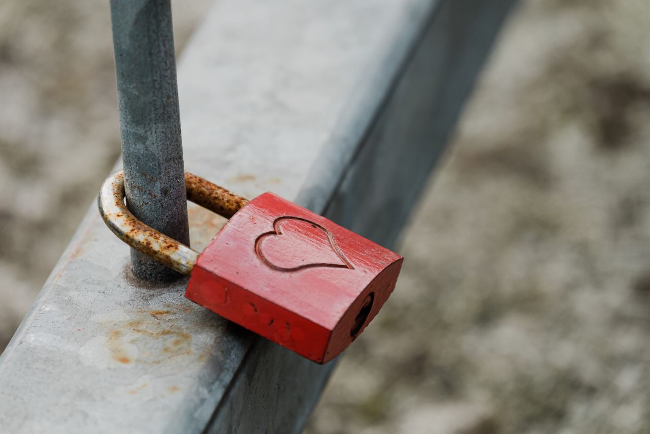 A closeup shot of a metal padlock with a heart hanging on a fence