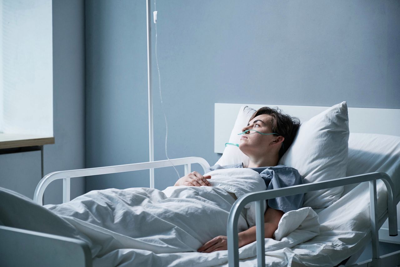 Sick young woman lying on the bed alone at hospital ward during pandemic