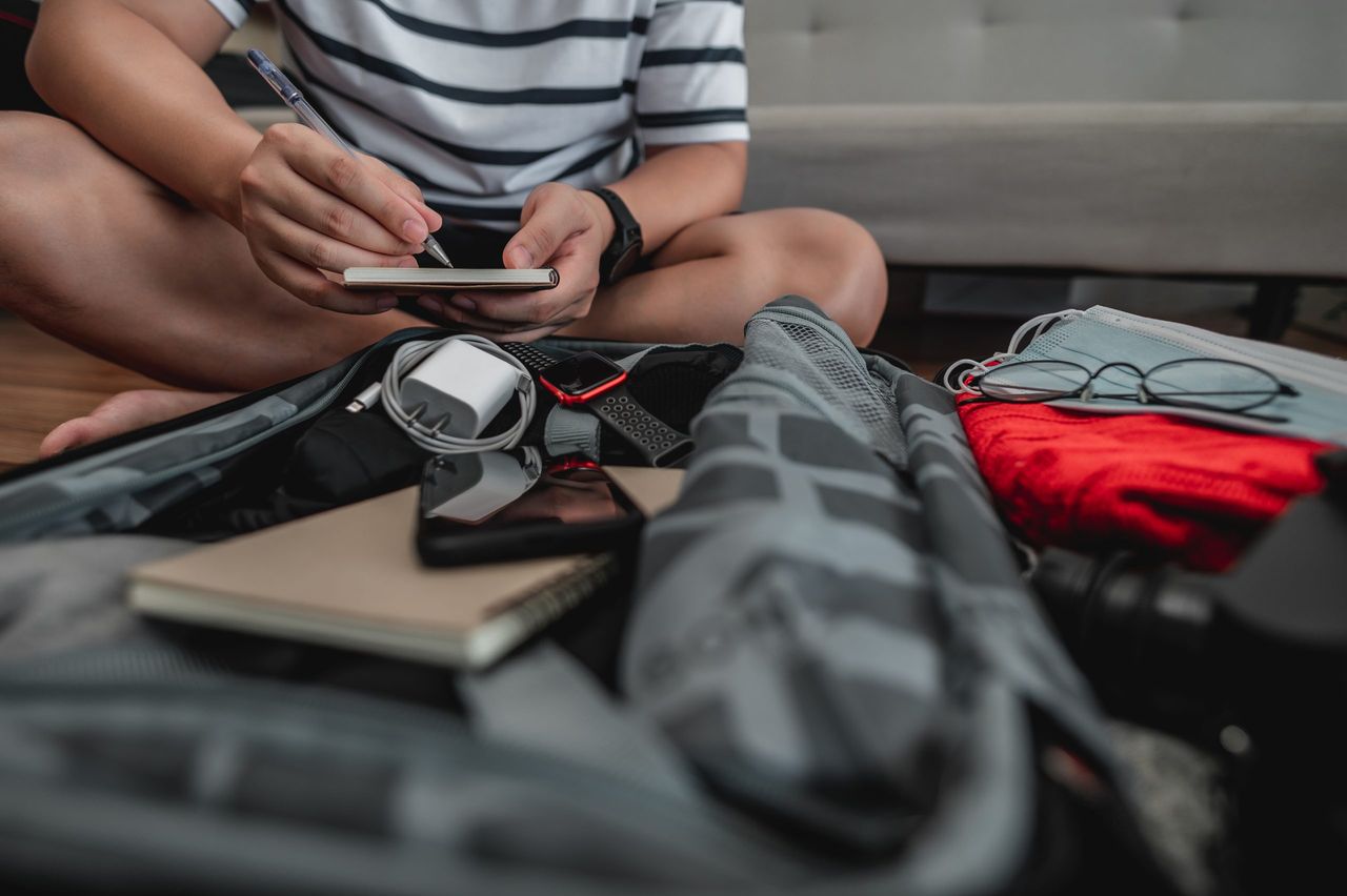 Asian man is preparing clothes in suitcases. He's choosing clothes, travel documents, the itinerary for a solo trip, and check the checklist. Travel, holiday and vacation concept.