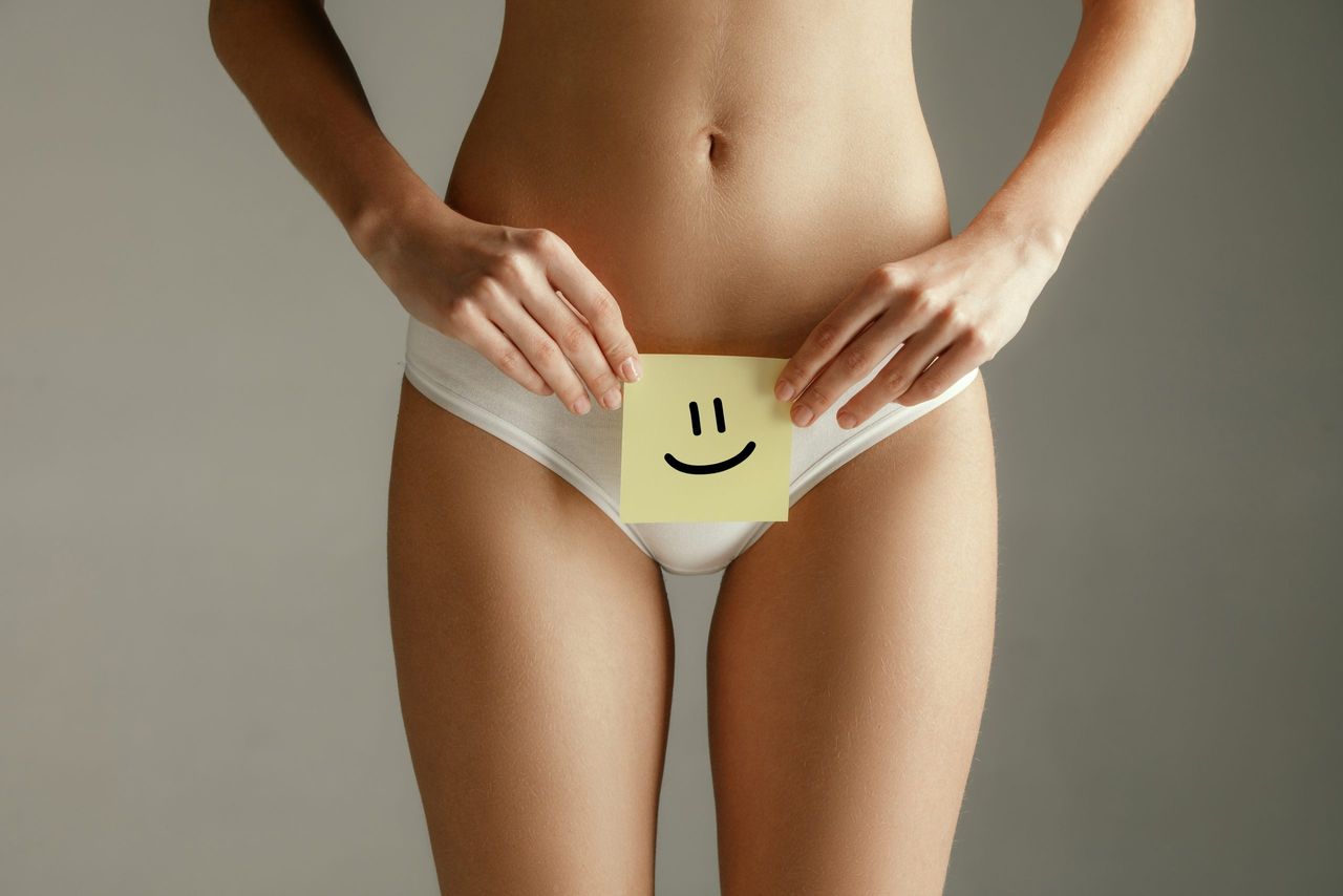 Woman health. Female model holding card near stomach. Young adult girl with paper sign or symbol of smile isolated on gray studio background. Cut out part of body. Medical problem and solution.
