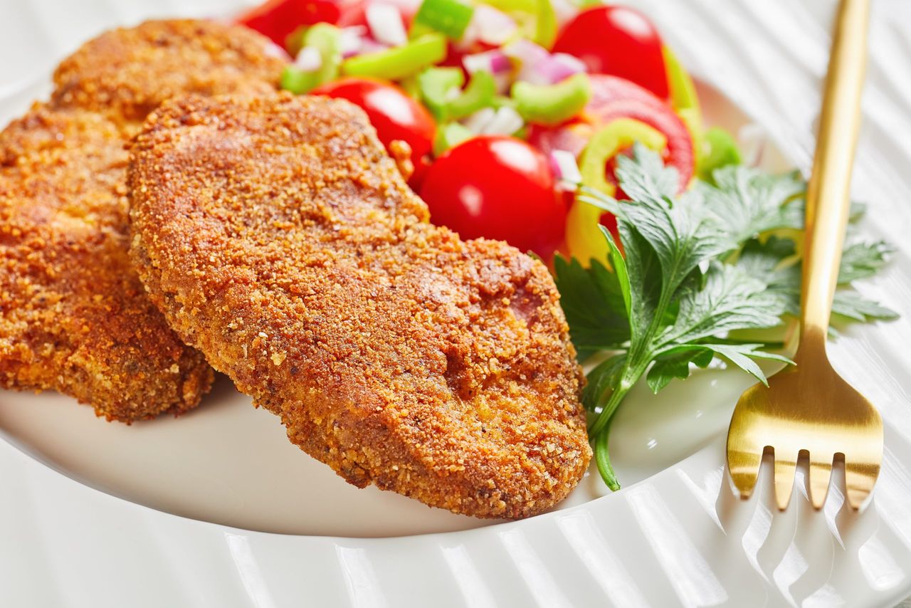 breaded lamb chops served with tomato, red onion, green pepper salad on a white plate on a wooden table, close-up